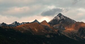 Breathtaking view of mountain peaks adorned with snow under a cloudy sky at dusk.